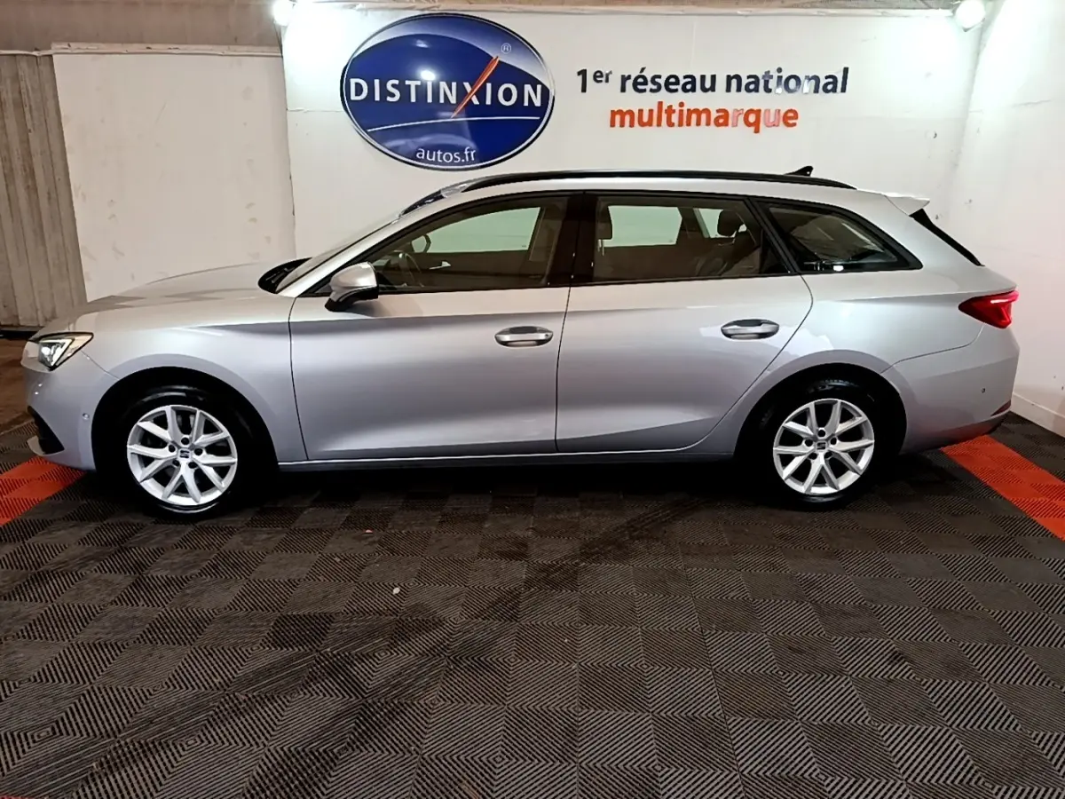 Vue de profil côté gauche d'une SEAT Leon break gris clair stationnée en intérieur sur sol noir et rouge.