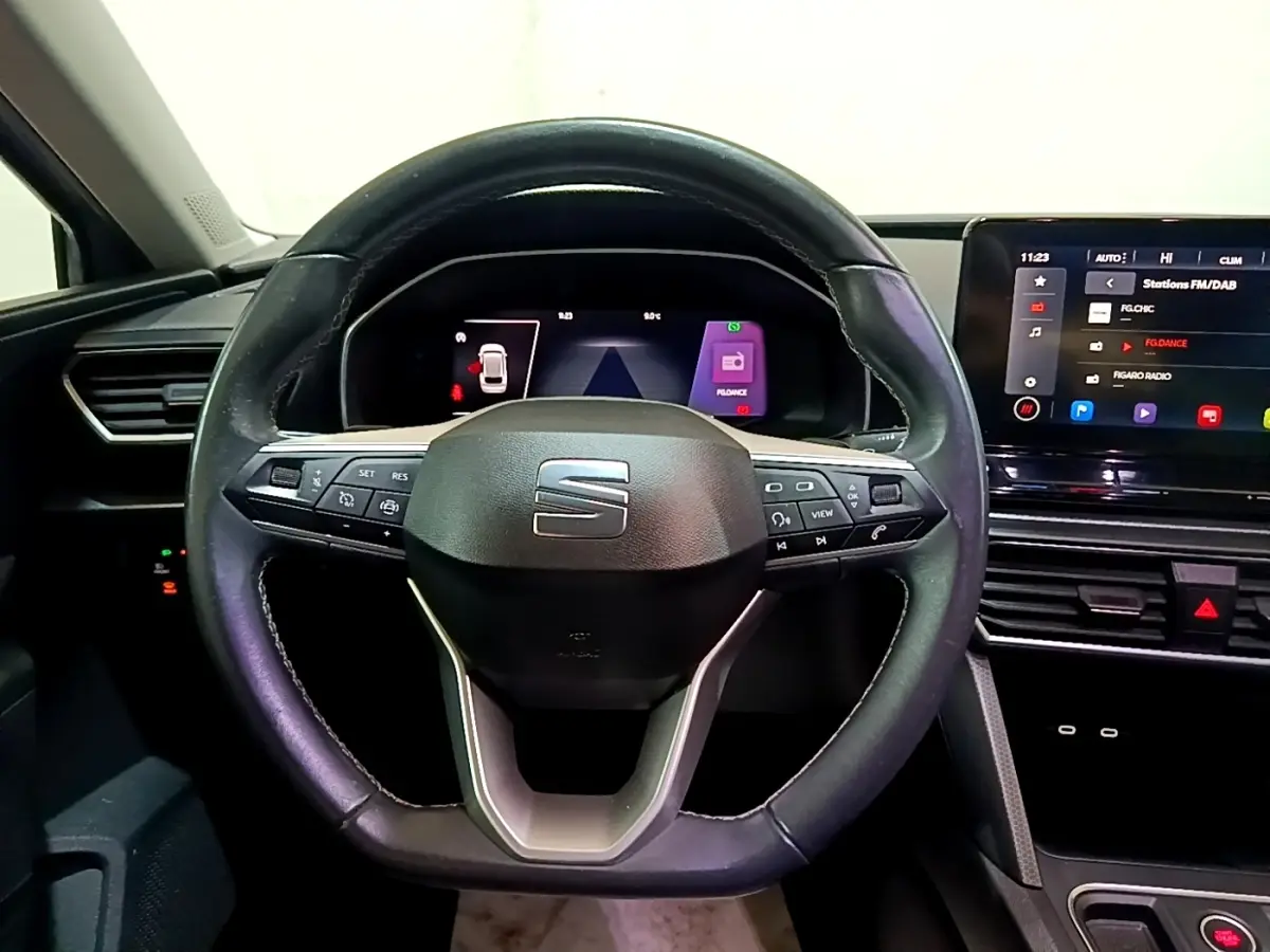 Vue intérieure centrée sur le volant cuir noir du SEAT Leon 2022 avec tableau de bord numérique et écran tactile.