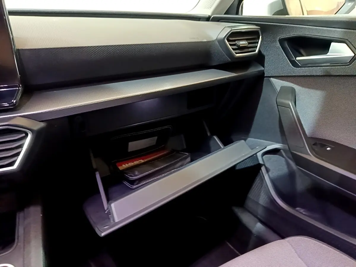 Intérieur côté passager du SEAT Leon gris foncé 2022, avec boîte à gants ouverte et tableau de bord moderne.
