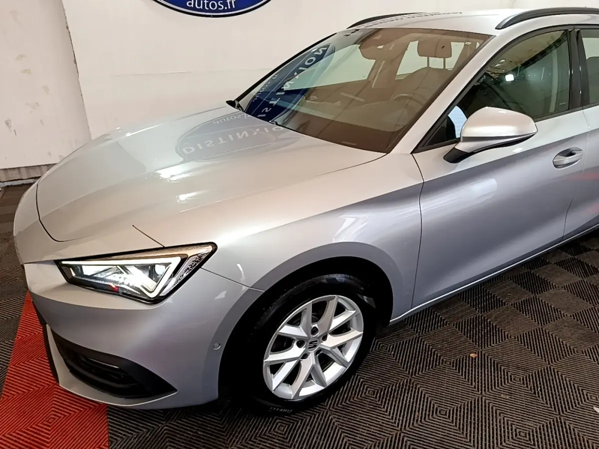 Vue 3/4 avant droit d'une SEAT Leon gris clair avec phares LED allumés dans un showroom.