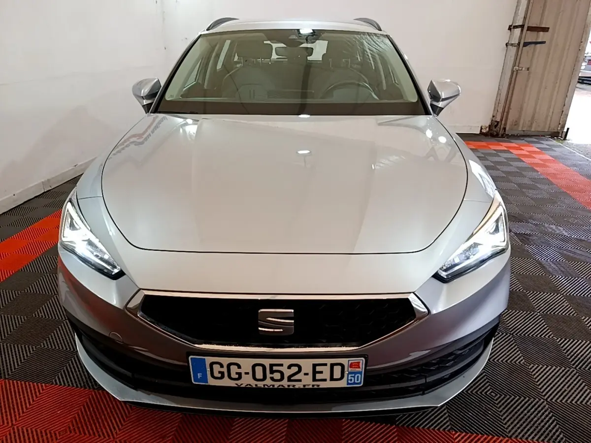 Vue avant d'une SEAT Leon gris foncé avec phares LED allumés, garée sur un sol à motifs rouges et noirs.