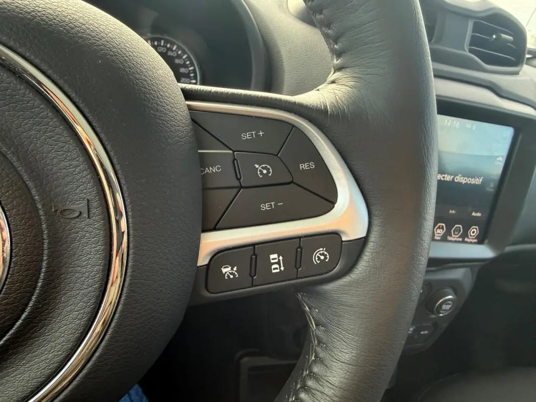 Gros plan sur le volant noir du Jeep Renegade 2023 avec commandes de régulateur de vitesse et écran tactile en arrière-plan.