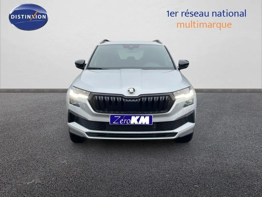 Vue de face du SUV SKODA KAROQ argent 2025 avec calandre noire et phares allumés sur fond neutre.