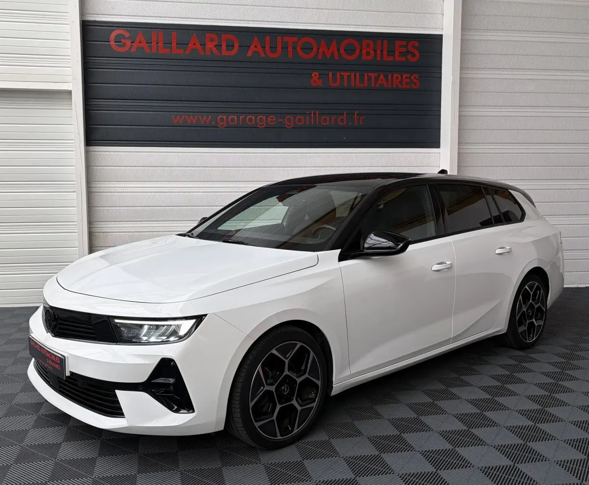 Opel Astra 2024 blanche vue 3/4 avant droit avec toit noir et jantes noires au showroom.