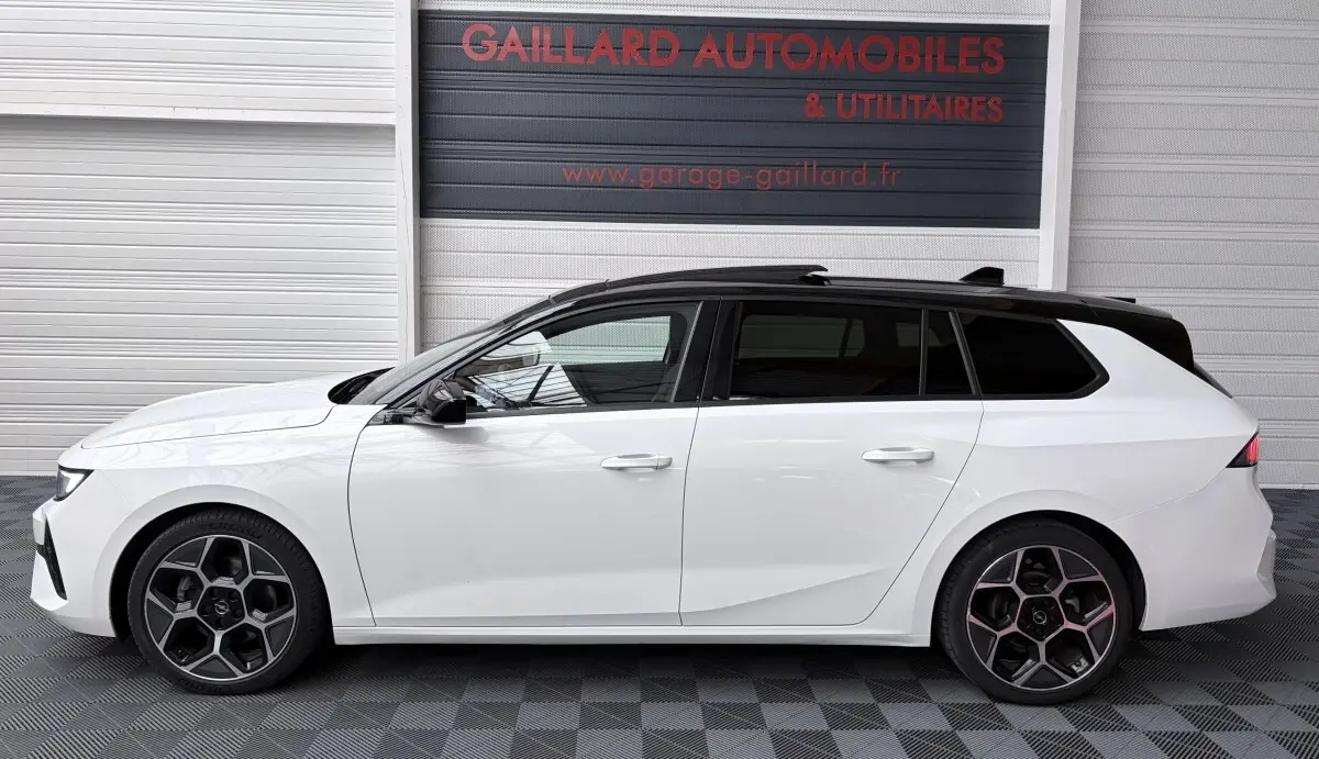 Vue latérale gauche d'une Opel Astra blanche avec toit noir et jantes alliage au design hexagonal.