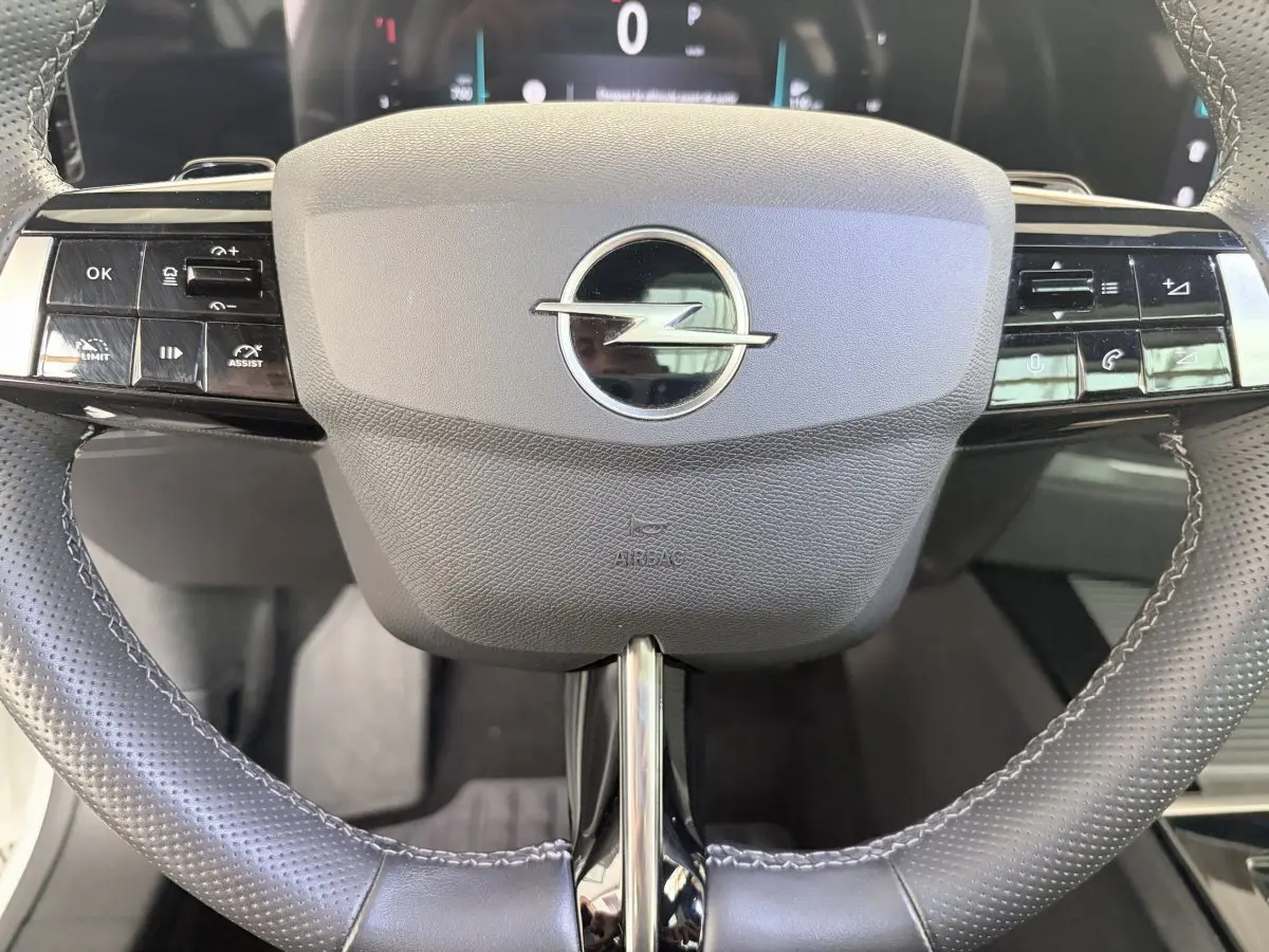 Gros plan sur le volant cuir noir perforé de l’Opel Astra 2024 avec commandes multifonctions et logo central chrome.