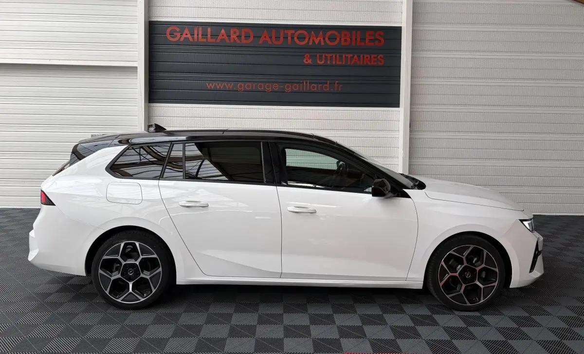 Vue latérale droite d'une Opel Astra blanche avec toit ouvrant noir, jantes alliage et vitres teintées.