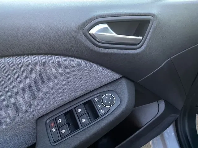 Gros plan sur la porte avant gauche gris clair de la Renault Clio 2025, avec commandes électriques des vitres et poignée argentée.