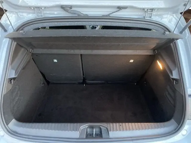 Coffre ouvert de la Renault Clio Techno TCe 90 gris clair, vue de l'arrière montrant l'espace de chargement et l'éclairage intérieur.