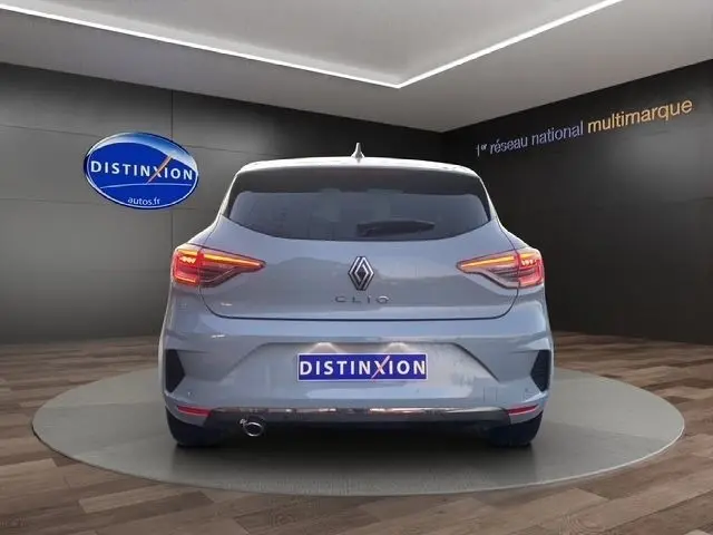 Vue arrière d'une Renault Clio gris clair 2025 dans un showroom avec feux LED allumés et logo distinctif au centre.