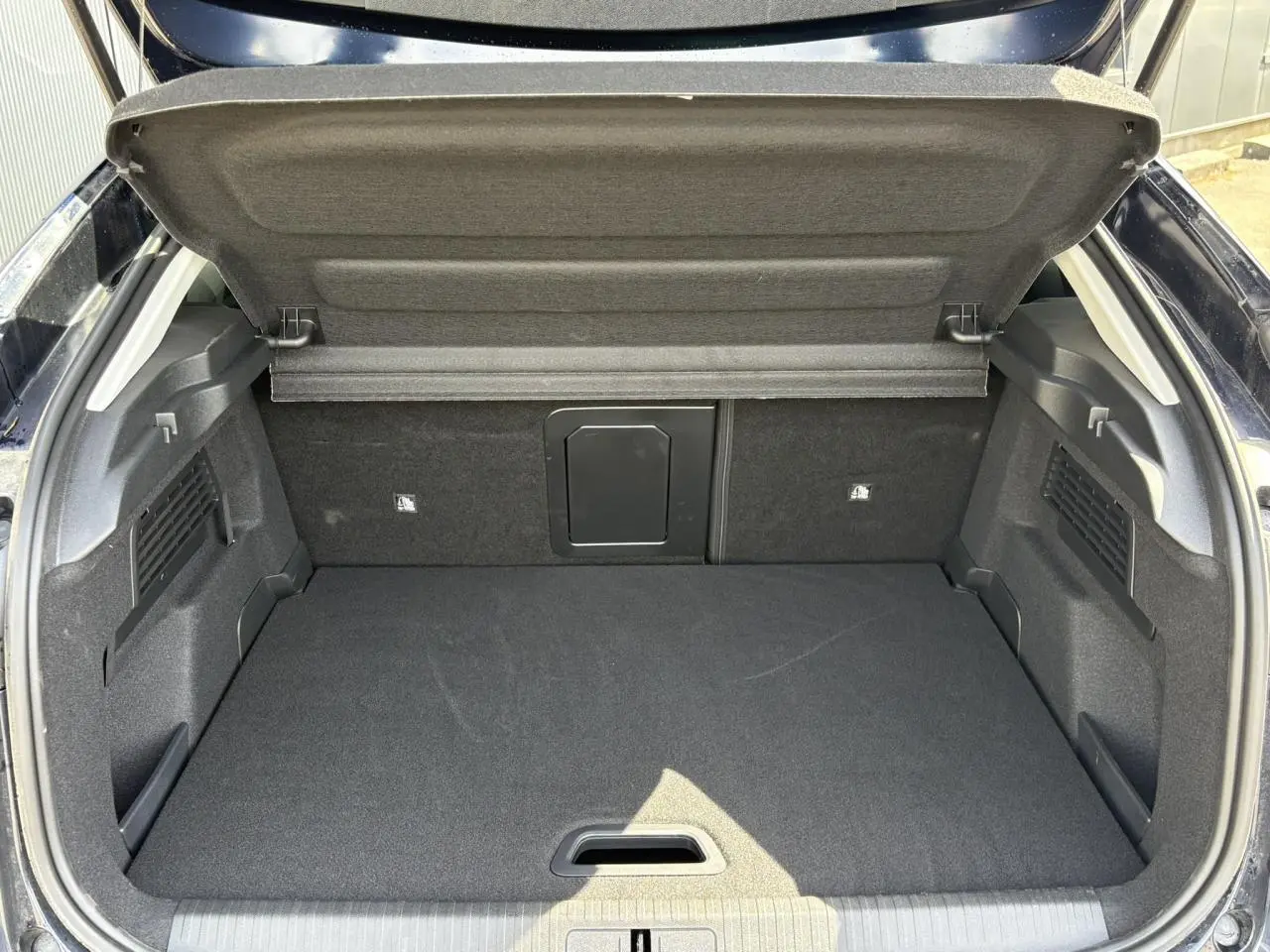 Coffre ouvert vu de l'arrière d'une Citroën C4 Hybrid 145 bleu Eclipse, espace de chargement vide et tapis noir.