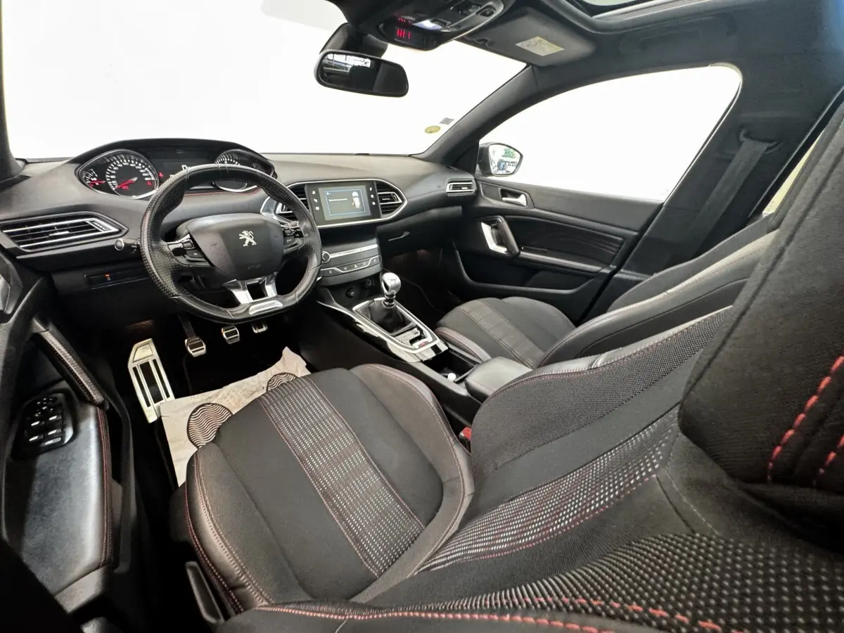 Intérieur de la Peugeot 308 GT Line 2018 vu côté conducteur, sièges noirs avec surpiqûres rouges et tableau de bord moderne.
