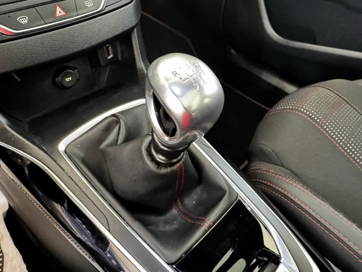 Gros plan sur le levier de vitesse manuel chromé et la console noire avec surpiqûres rouges du siège avant droit de la Peugeot 308.