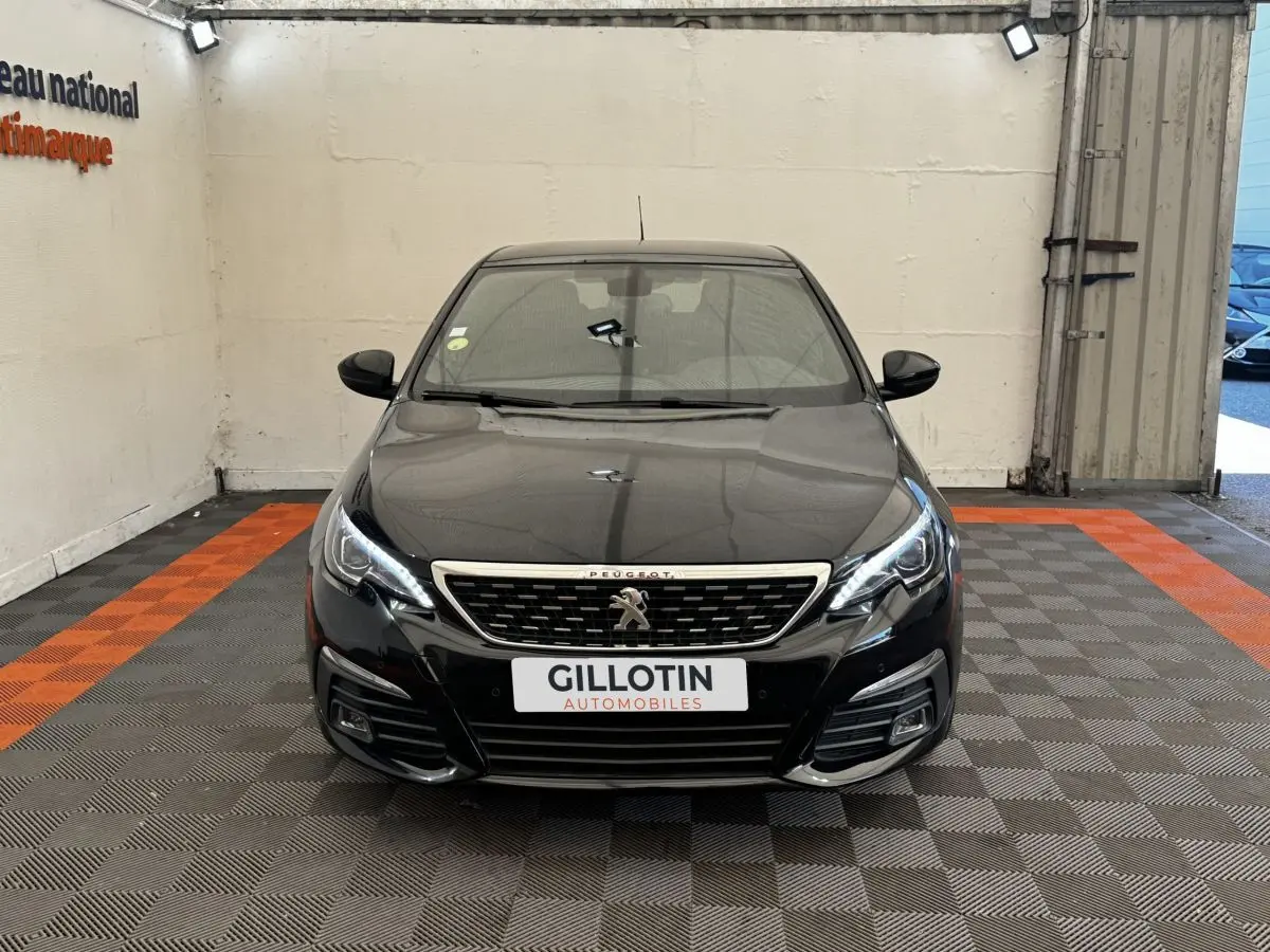 Vue avant frontale d'une Peugeot 308 noire avec calandre chromée et feux LED allumés dans un garage.