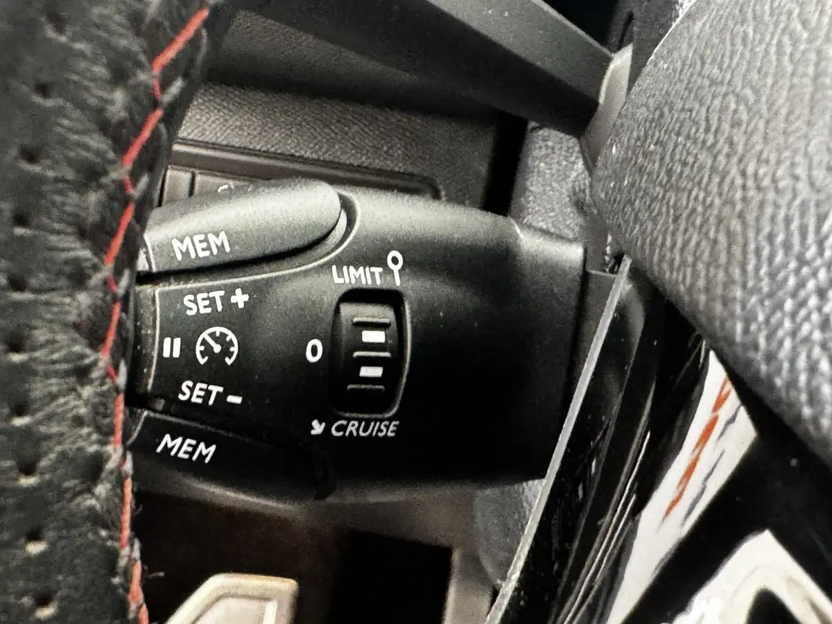 Gros plan sur la commande de régulateur de vitesse noire, avec volant cuir noir et surpiqûres rouges visible, Peugeot 308.