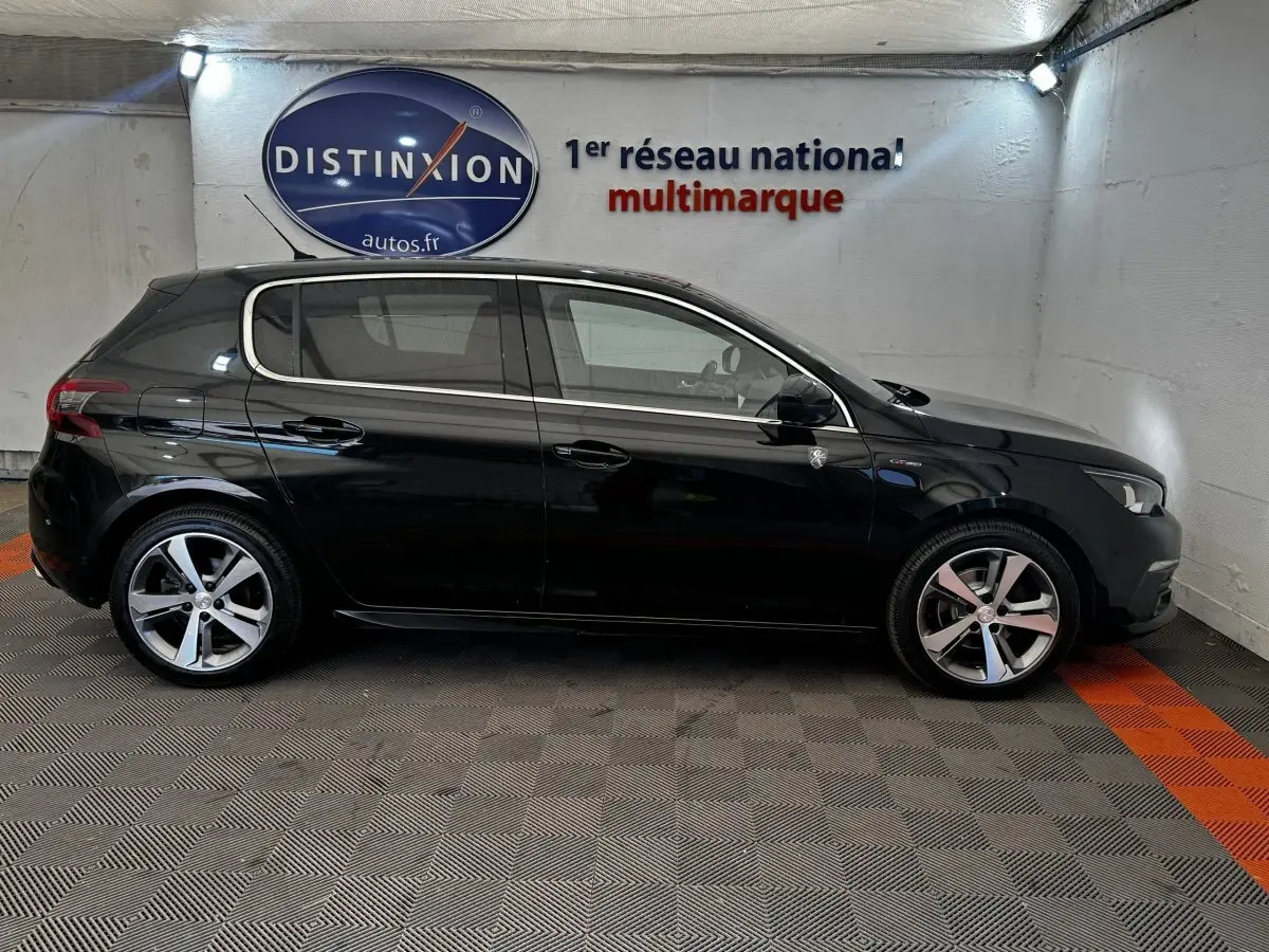 Peugeot 308 GT Line noire vue de profil côté gauche dans un garage avec sol gris et orange.