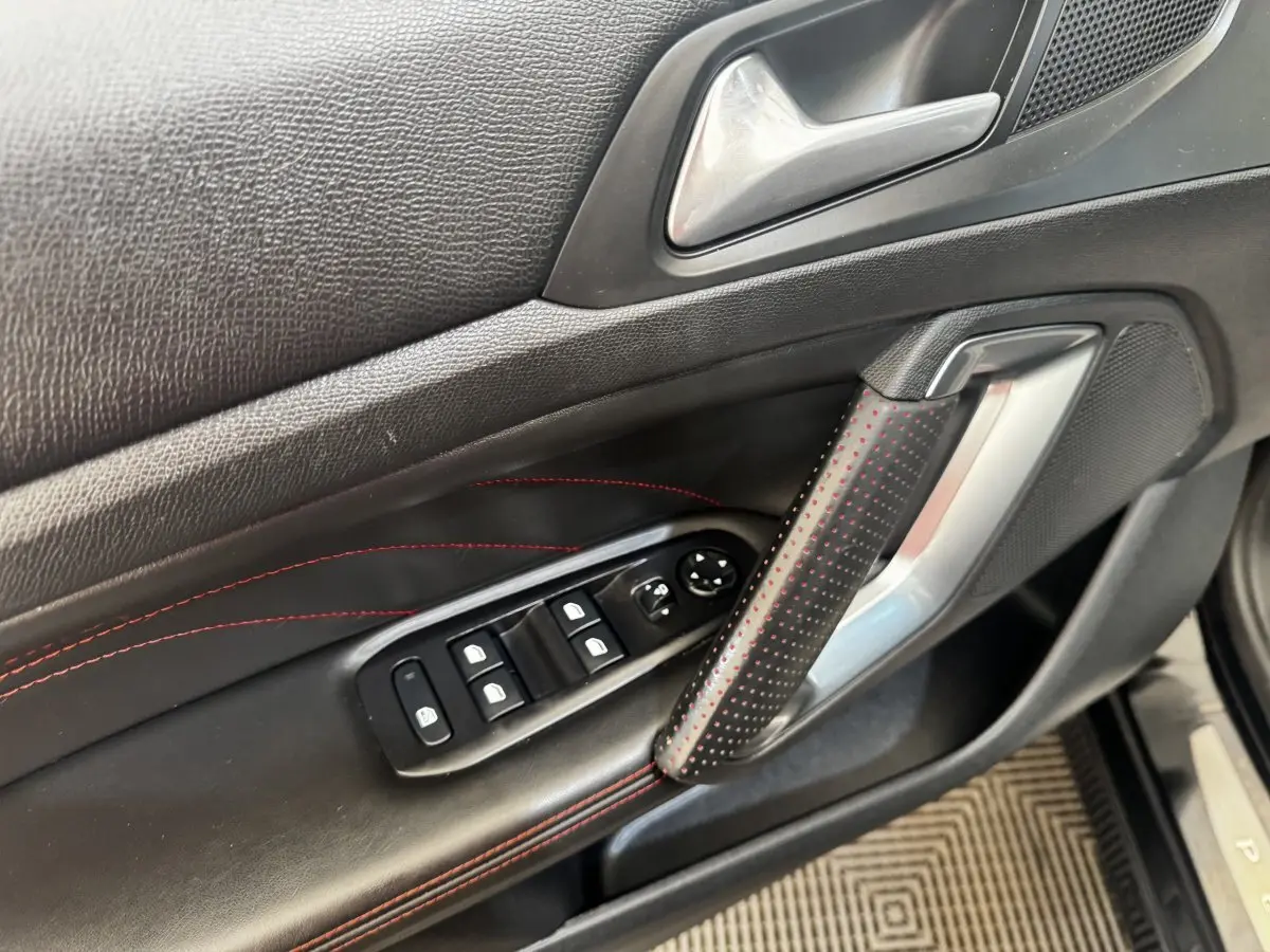 Gros plan sur la porte intérieure côté conducteur de la Peugeot 308 noire, avec surpiqûres rouges et commandes des vitres.