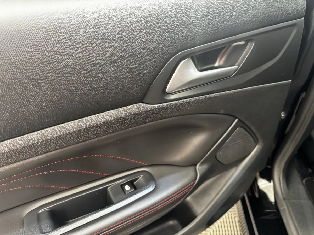 Détail de la porte avant gauche noire de la Peugeot 308 GT Line avec surpiqûres rouges et poignée argentée.