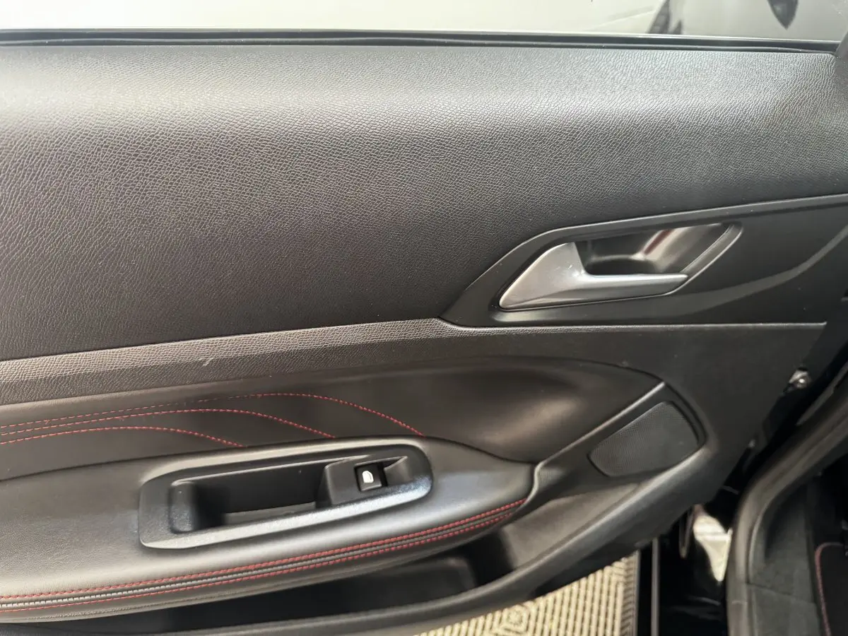 Intérieur côté gauche de la porte avant d’une Peugeot 308 noire, avec surpiqûres rouges et poignée argentée.
