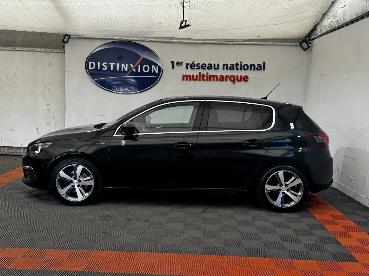 Vue de profil côté gauche d'une Peugeot 308 noire GT Line 2018 dans un showroom avec sol à damier gris et orange.