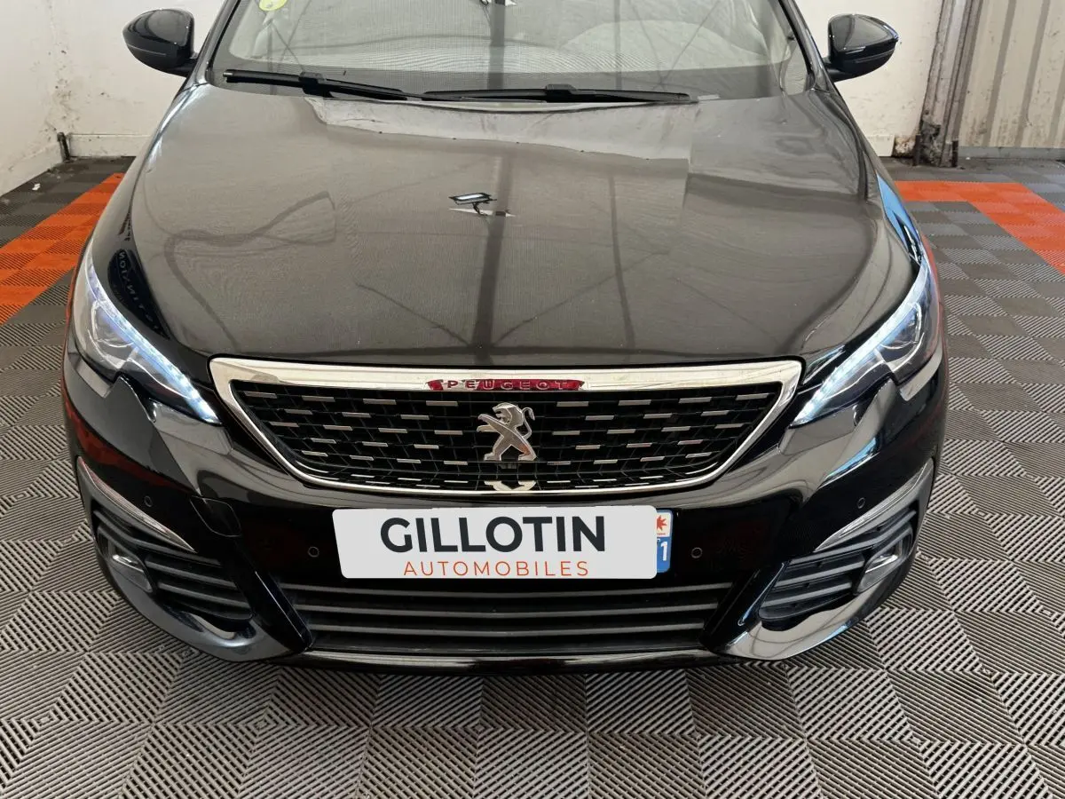 Vue avant rapprochée de la Peugeot 308 noire avec calandre chromée et feux LED allumés sur sol damier.
