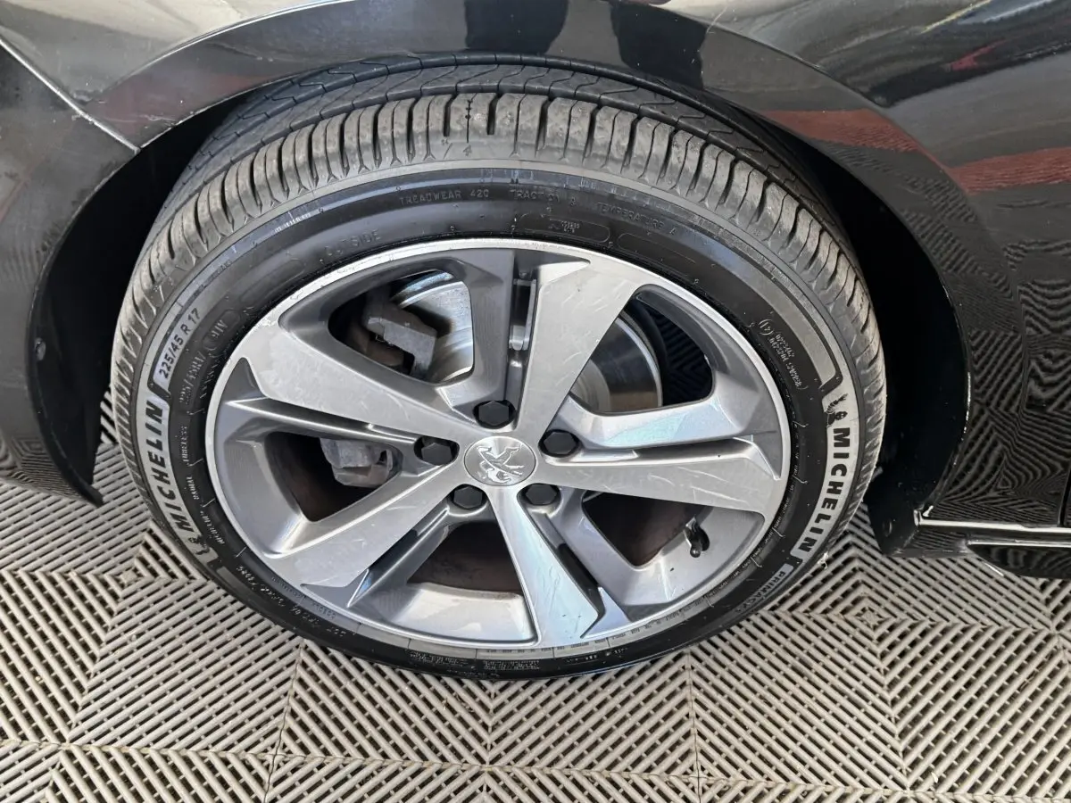 Gros plan sur la roue avant droite de la Peugeot 308 noire, jante alliage à cinq branches doubles, pneu Michelin.