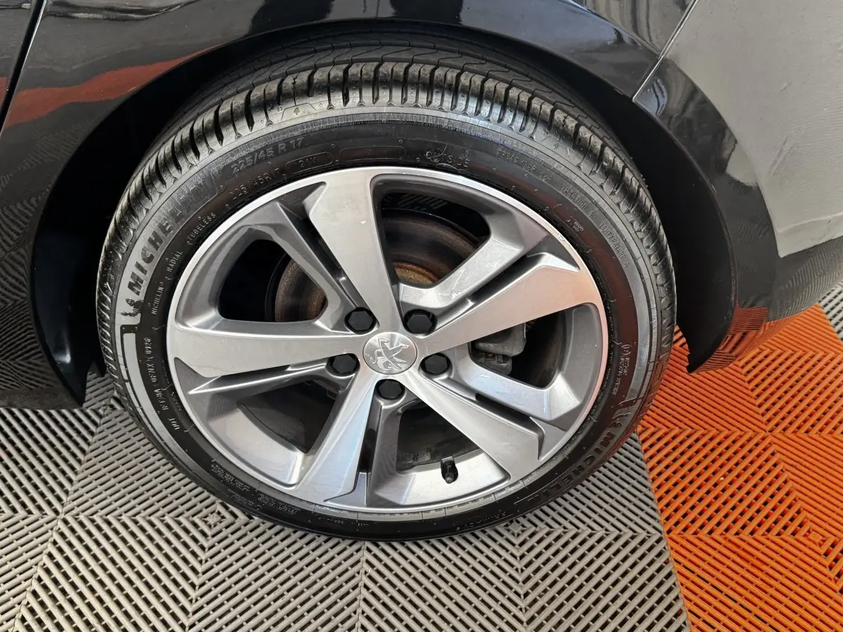 Gros plan sur la roue avant droite noire d’une Peugeot 308 1.5 BlueHDi 130 S&S GT Line avec jante alliage grise.