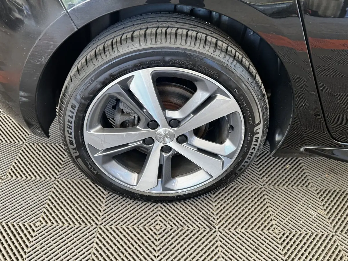 Gros plan sur la roue avant gauche de la Peugeot 308 noire, avec jante alliage et pneu Michelin visible.