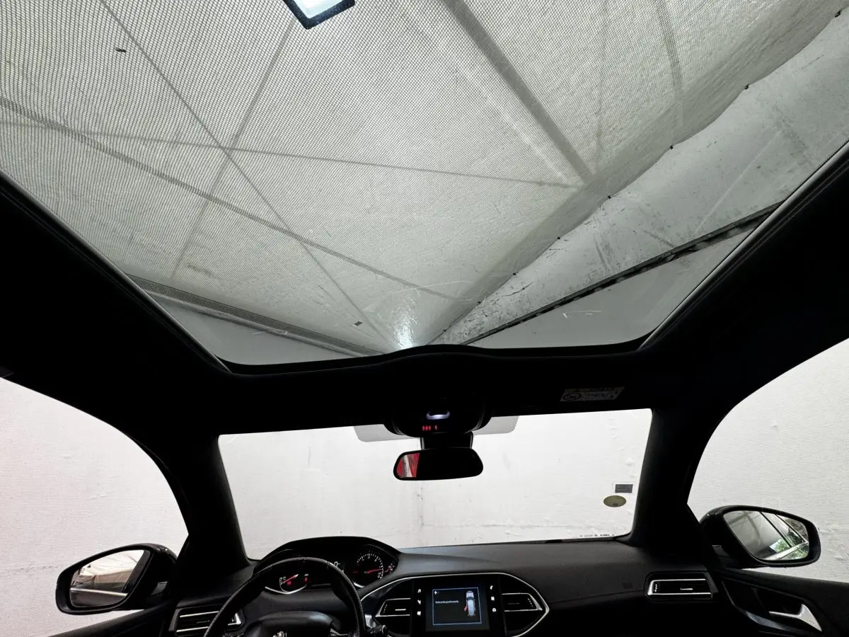Vue intérieure avant du Peugeot 308 noir 2018, avec toit panoramique et tableau de bord digital lumineux.