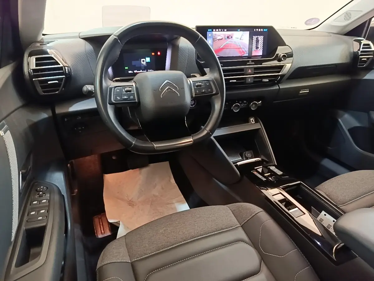 Vue intérieure avant du Citroën C4 X noir 2023, volant cuir multifonctions et écran tactile central affichant la caméra de recul.
