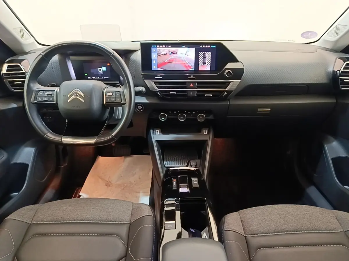 Vue intérieure frontale du tableau de bord et volant cuir noir du Citroën C4 X 2023 avec écran tactile central allumé.