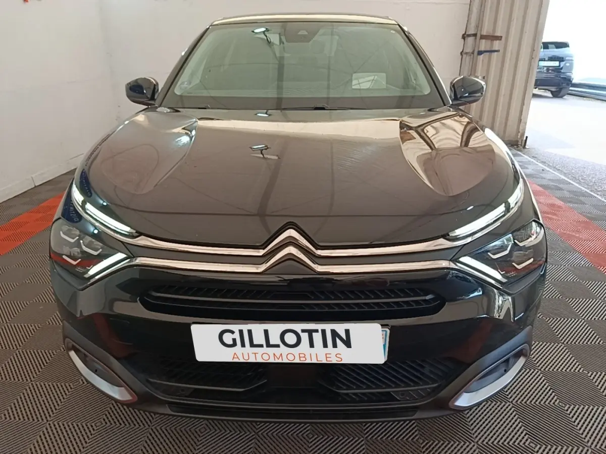 Vue frontale d'une Citroën C4 X noire 2023 avec phares LED et calandre chromée dans un garage.