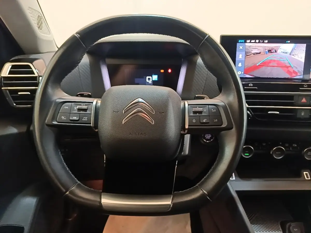 Vue intérieure centrée sur le volant cuir noir de la Citroën C4 X 2023 avec écran tactile de navigation affichant la caméra de recul.