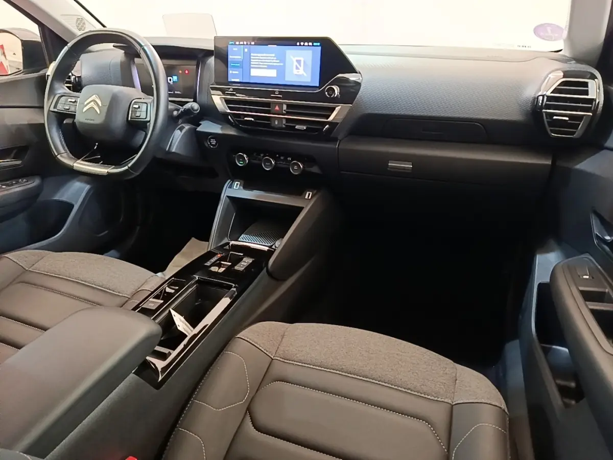 Intérieur avant du Citroën C4 X 2023, vue côté conducteur, tableau de bord noir avec écran tactile central.