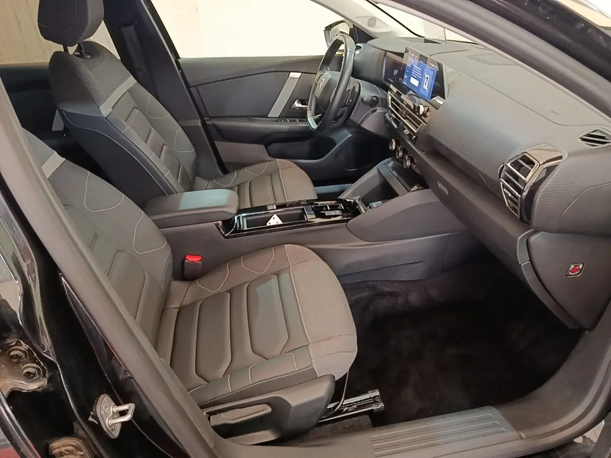 Vue intérieure côté conducteur de la Citroën C4 X noire 2023, avec sièges tissu et tableau de bord moderne.