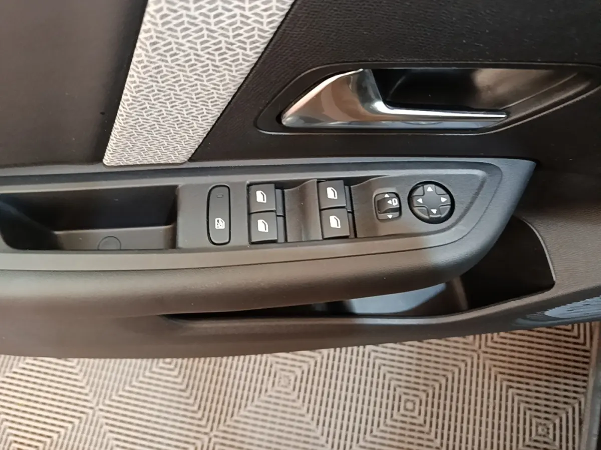 Gros plan sur la commande des vitres et rétroviseurs côté conducteur d'une Citroën C4 X noire, intérieur tissu gris.