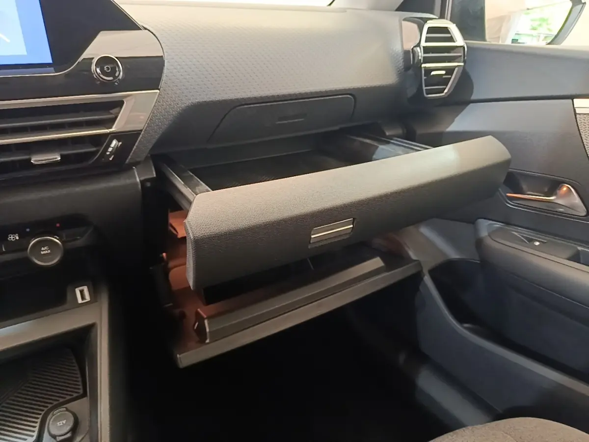 Vue intérieure côté passager du tableau de bord noir du Citroën C4 X avec boîte à gants ouverte et détails de la console.