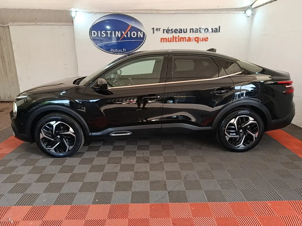 Profil côté gauche d'une Citroën C4 X noire 2023, avec jantes distinctives et toit panoramique en intérieur showroom.