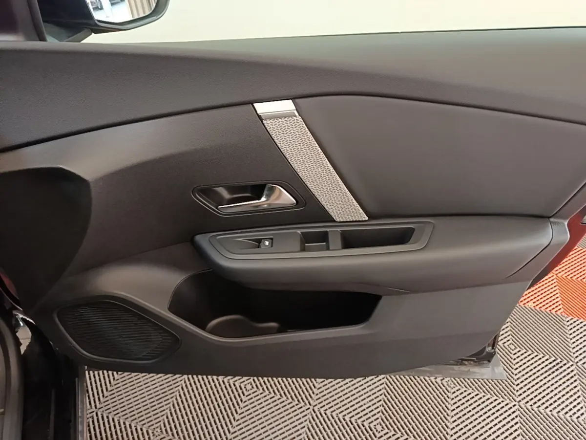 Intérieur côté gauche de la porte noire du Citroën C4 X 2023 avec poignée chromée et haut-parleur intégré.