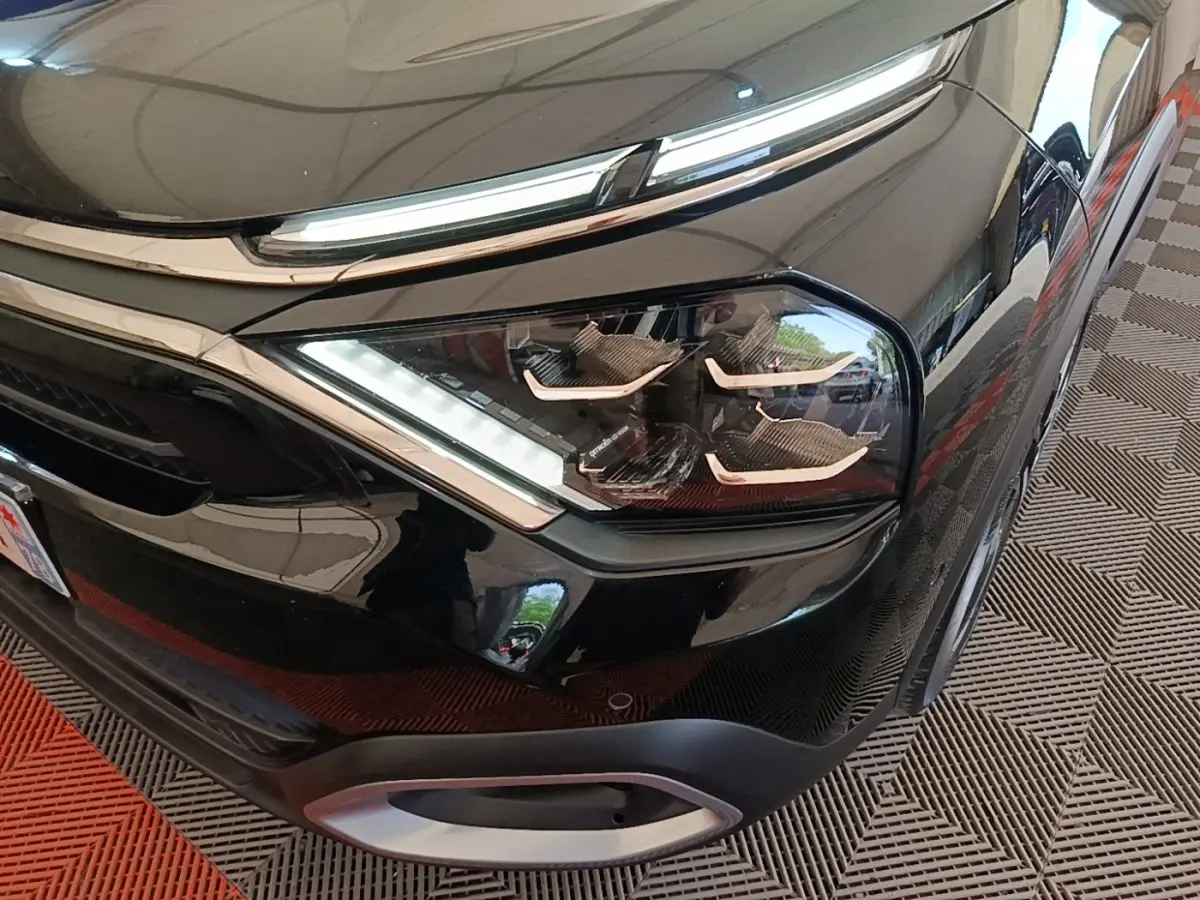 Gros plan sur le phare avant droit noir brillant du Citroën C4 X 2023 avec détails LED et calandre chromée.