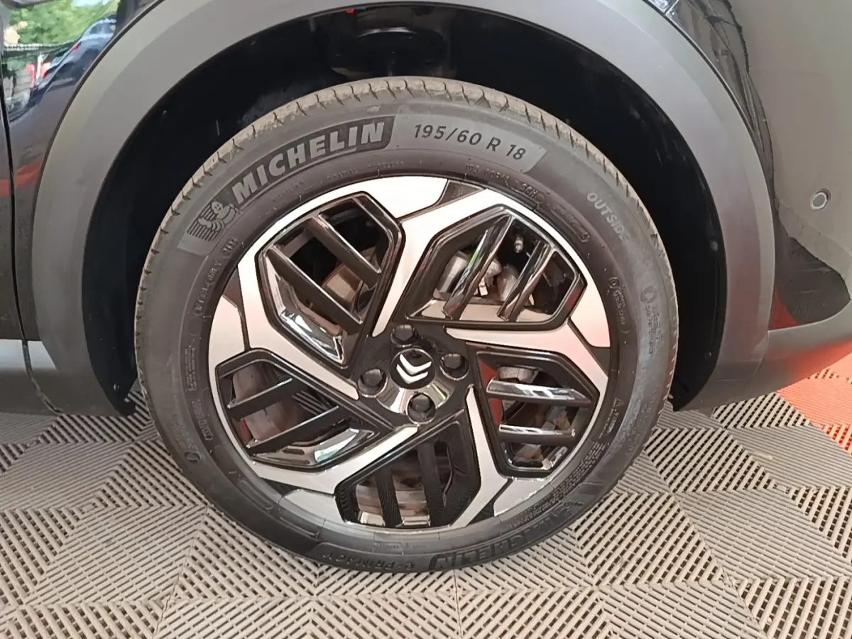 Gros plan sur la roue avant droite noire d'une Citroën C4 X 2023 avec jante alliage au design géométrique.