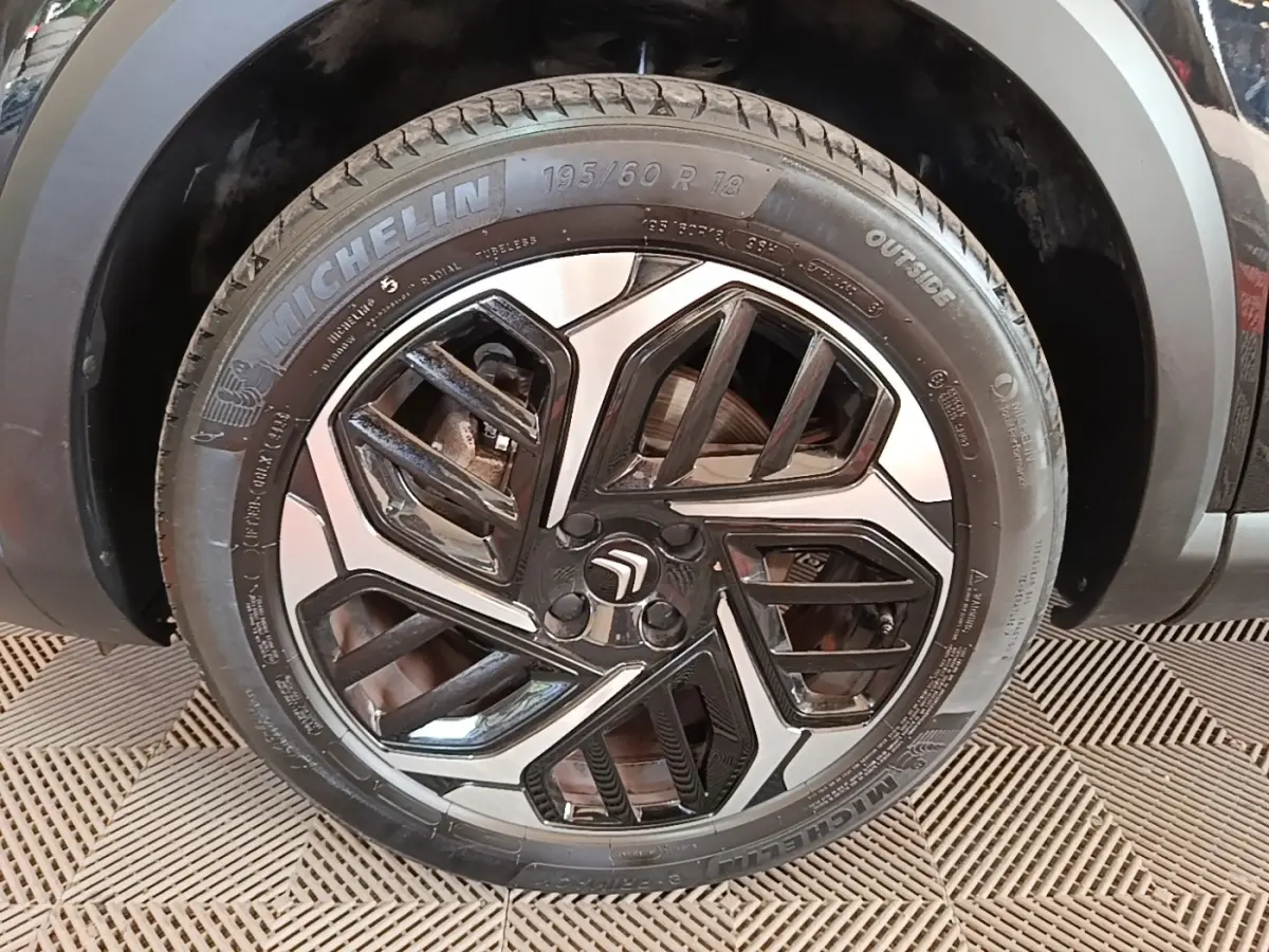 Gros plan sur la roue avant gauche noire d'une Citroën C4 X 2023 avec jante alliage bicolore et pneu Michelin.