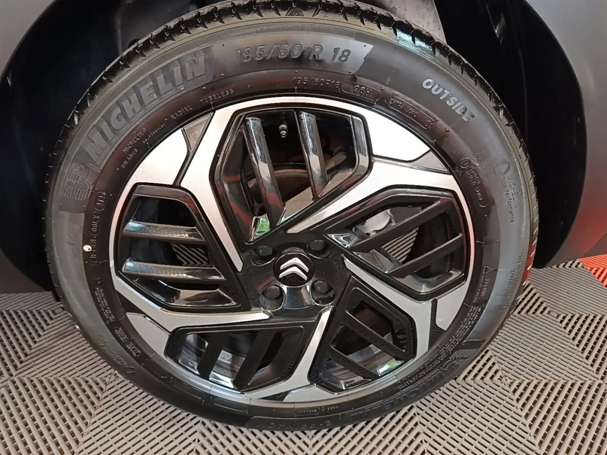 Gros plan sur la roue avant gauche noire avec jante alliage bicolore et logo Citroën au centre.