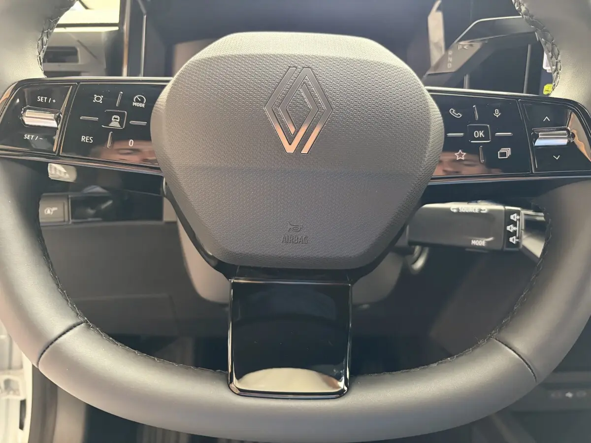 Gros plan sur le volant noir de la Renault Clio 2026 avec commandes intégrées et logo Renault central.