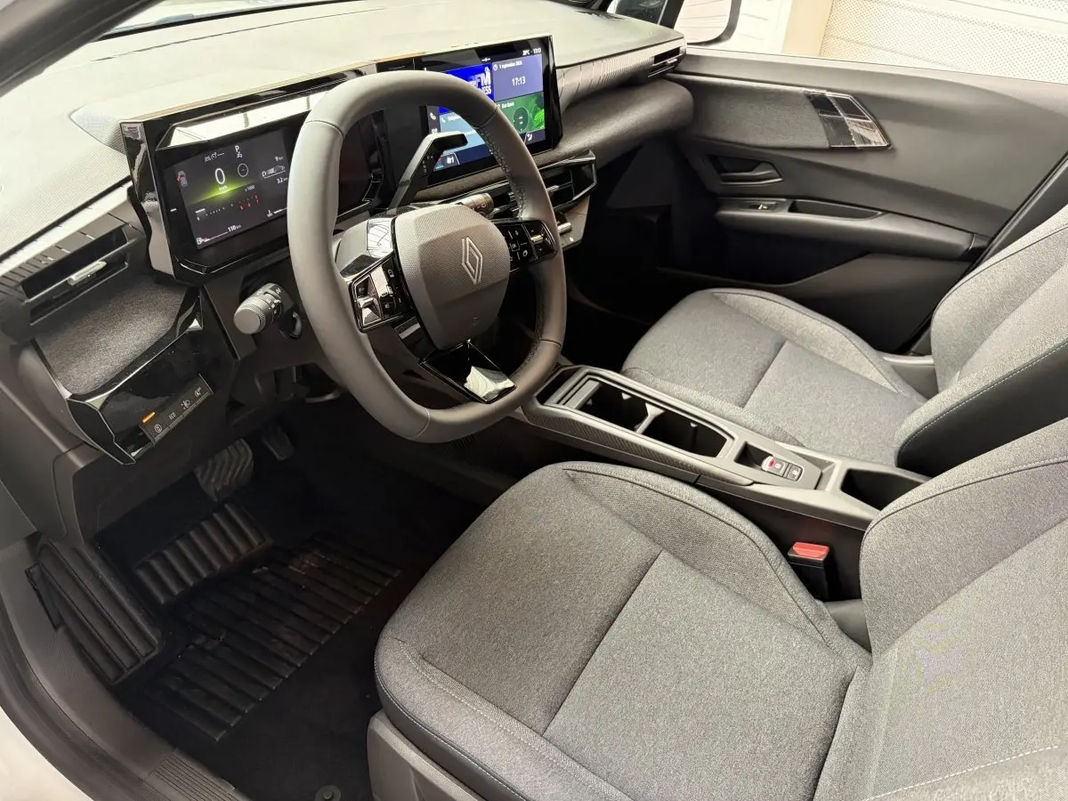 Intérieur de la Renault Clio 2026 blanc, vue côté conducteur, tableau de bord numérique et sièges gris tissu.