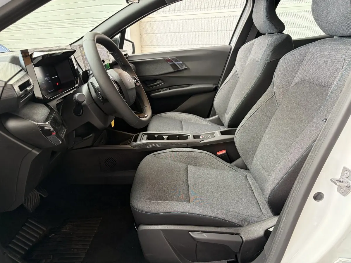 Intérieur avant droit de la Renault Clio 2026 blanche, sièges tissu gris et tableau de bord moderne avec écran tactile.