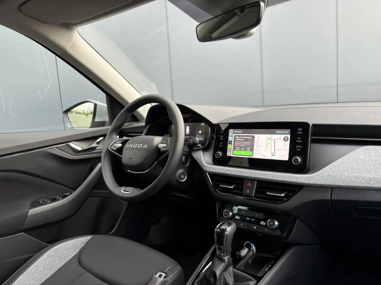 Intérieur avant droit du Skoda Kamiq 2025, tableau de bord gris clair avec écran tactile et volant multifonctions noir.