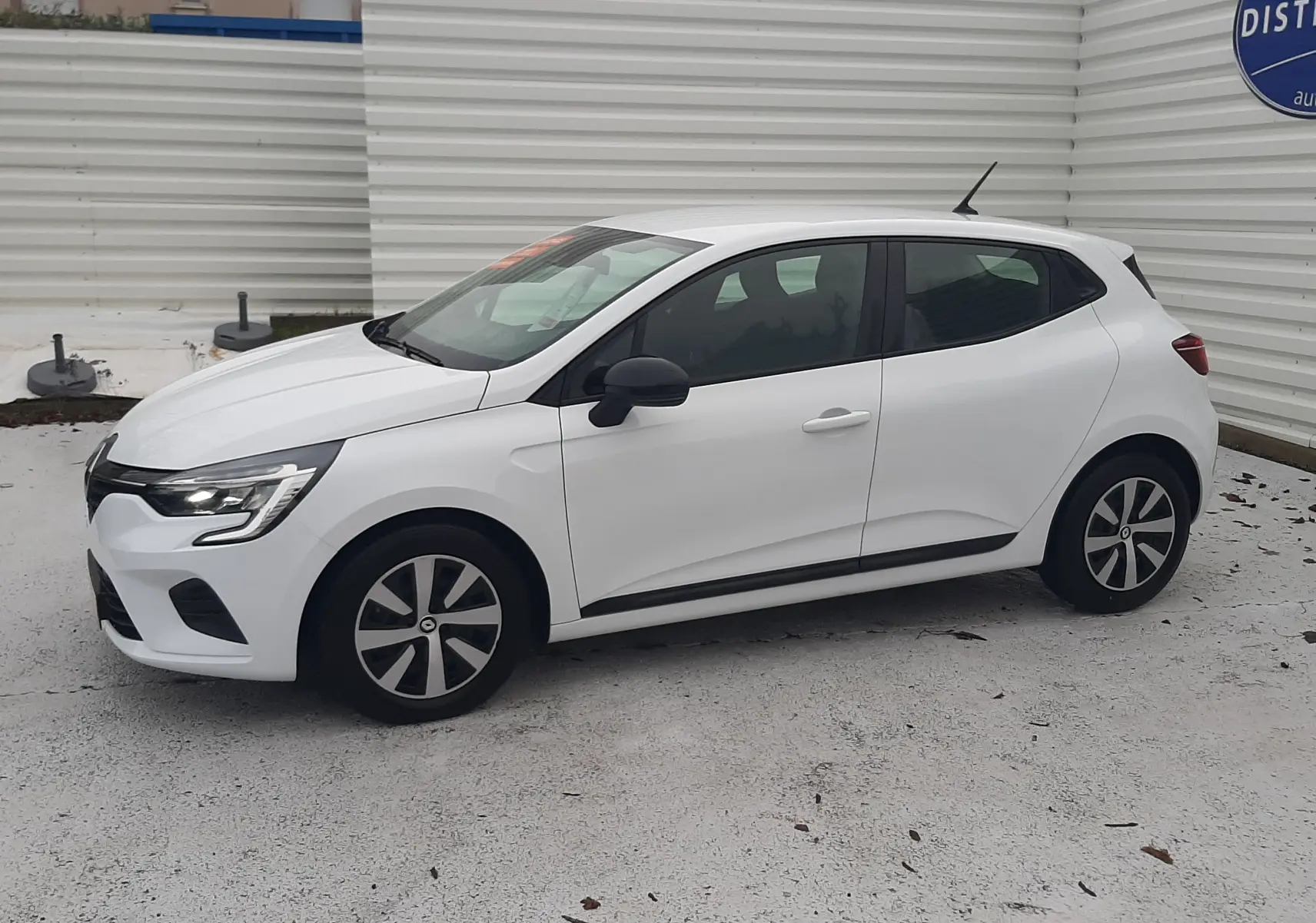 Renault Clio V blanche vue de profil côté gauche, avec jantes noires et détails noirs sur les rétroviseurs et bas de caisse.