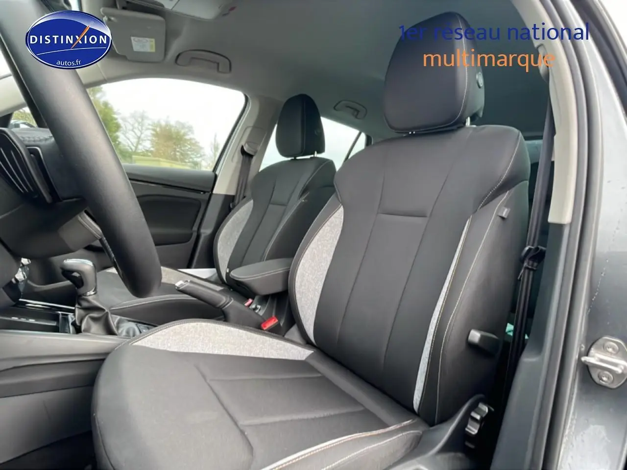 Vue intérieure côté avant droit du Skoda Kamiq gris, mettant en valeur les sièges bi-matière et l'accoudoir central.