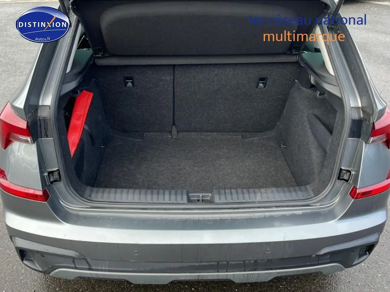 Coffre ouvert vu de l'arrière d'un Skoda Kamiq gris avec intérieur de coffre en tissu noir et triangle de sécurité rouge.